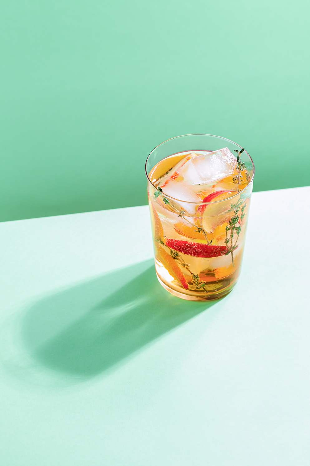 Sparkling cold brew peach tea with thyme in glass on green paper background